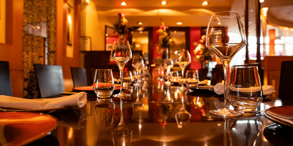Long restaurant table set with wine glasses and napkins under warm amber lighting
