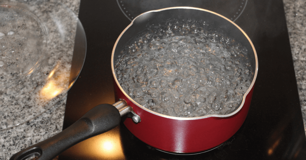 Water boiling hard in a red saucepan on a glass cooktop
