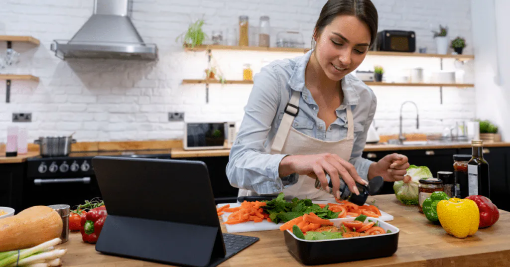 Woman preparing salmon and vegetables in her kitchen while following a recipe on a tablet