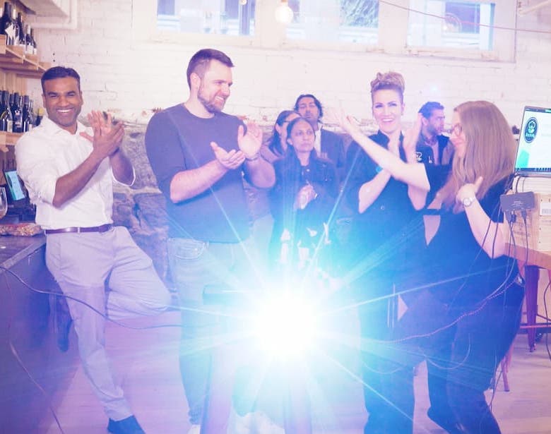 Colleagues clapping and laughing together at an indoor event, lit by a bright burst of light