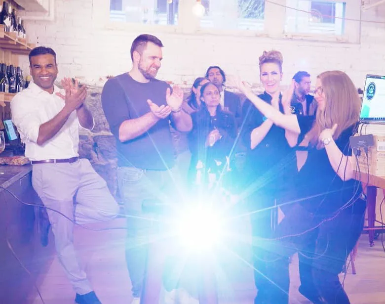 Colleagues clapping and laughing together at an indoor event, lit by a bright burst of light