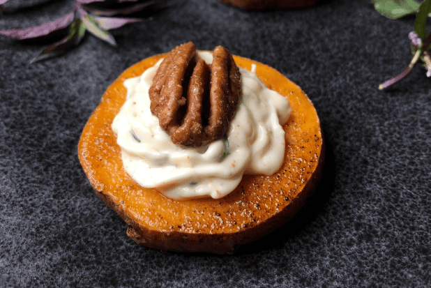 Roasted sweet potato round topped with piped white cream and a candied pecan on a slate board
