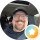 Paul Brinson grinning in a cap and glasses in the driver's seat of a car