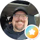 Paul Brinson grinning in a cap and glasses in the driver's seat of a car