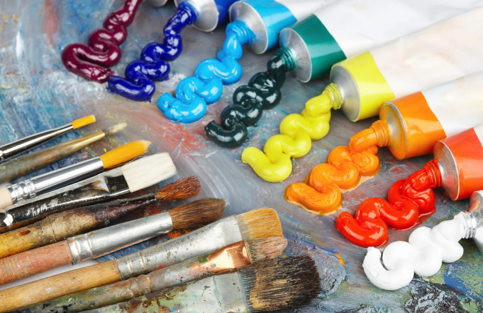 Rows of rainbow acrylic paint squeezed from tubes onto a palette beside well-used brushes