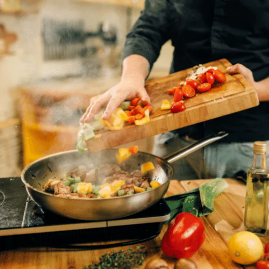 Cook tipping chopped peppers and vegetables from a wooden board into a steaming skillet
