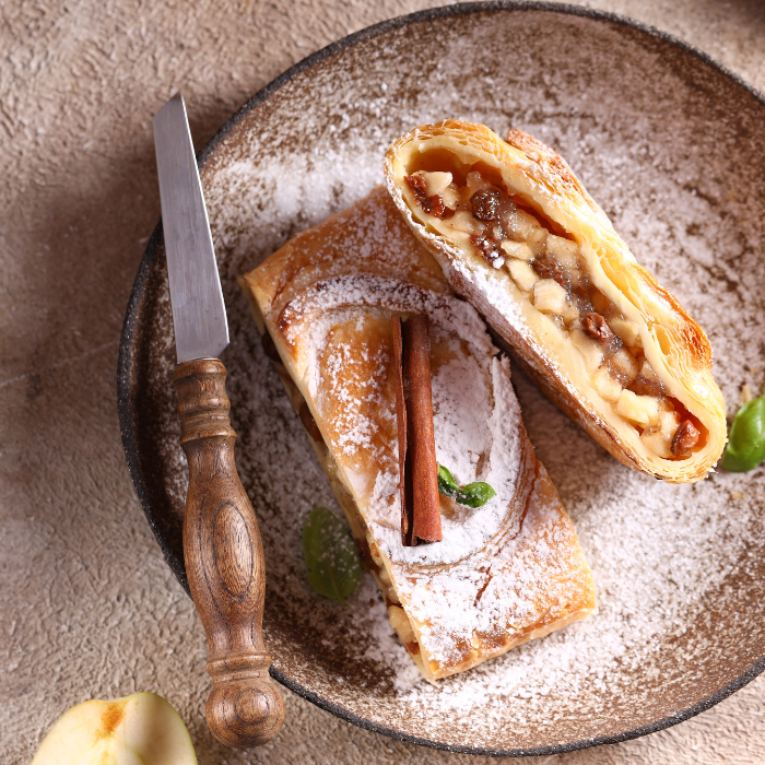 Sliced apple strudel dusted with powdered sugar showing the apple filling, with a cinnamon stick