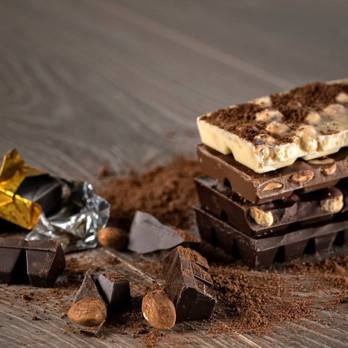 Stack of milk, dark and white chocolate bars with nuts, broken pieces and dusted cocoa powder