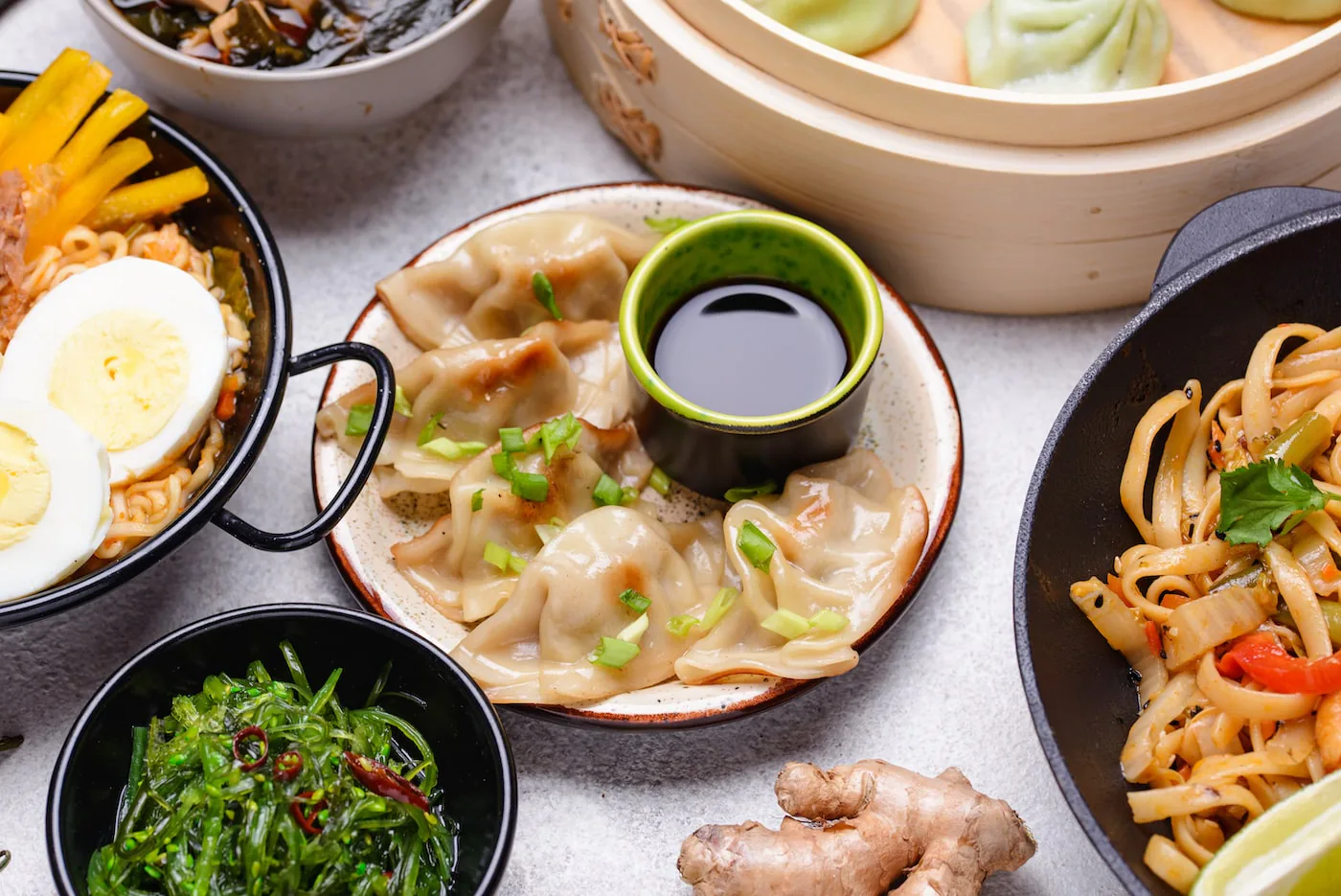Spread of Asian dishes including dumplings with soy sauce, ramen with egg, seaweed salad and wok noodles