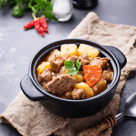 Beef stew with potatoes, carrots and parsley in a small black pot on a burlap cloth