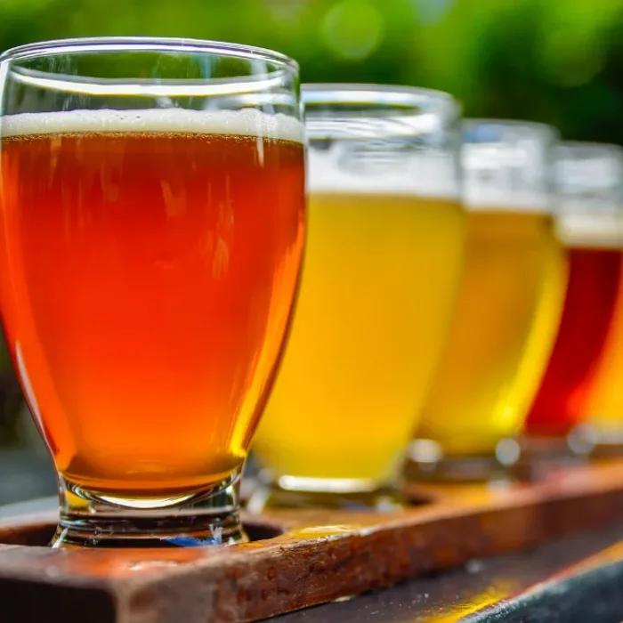 Flight of four craft beers from amber to golden to red on a wooden paddle outdoors