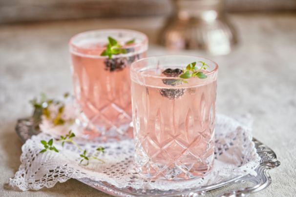 Two pink spritzers in cut-crystal tumblers garnished with blackberries and thyme on a silver tray