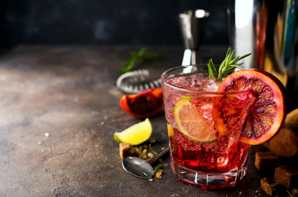 Deep red cocktail on ice garnished with a blood orange wheel, lemon slice and a rosemary sprig