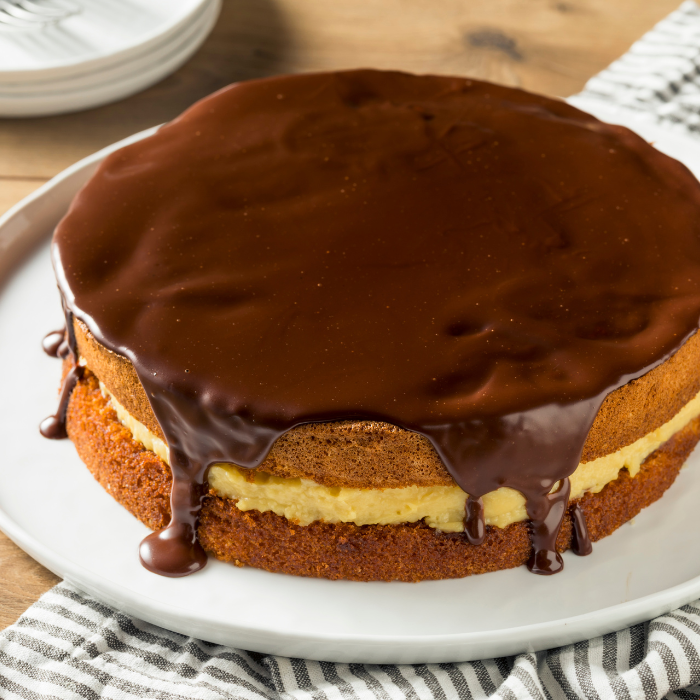 Boston cream pie with a custard-filled sponge under thick chocolate glaze dripping down the sides