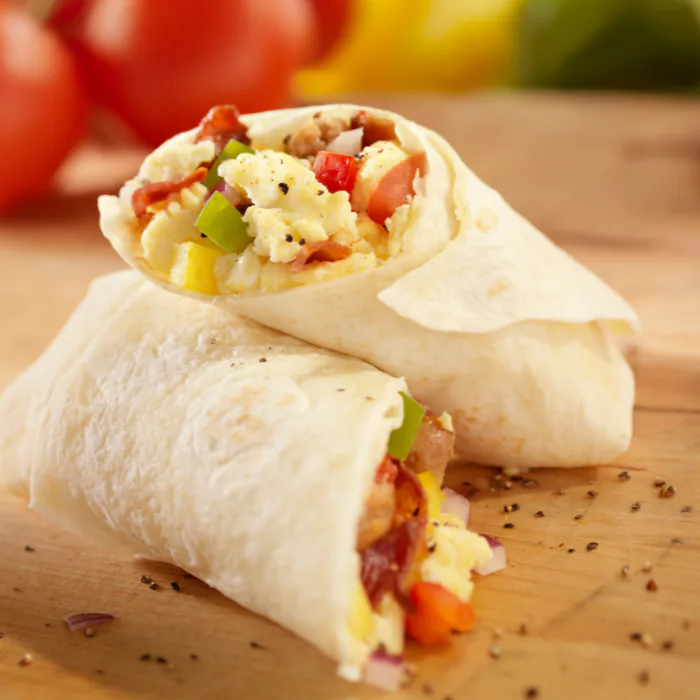 Two breakfast burritos cut open to show scrambled egg, peppers and tomato on a wooden board