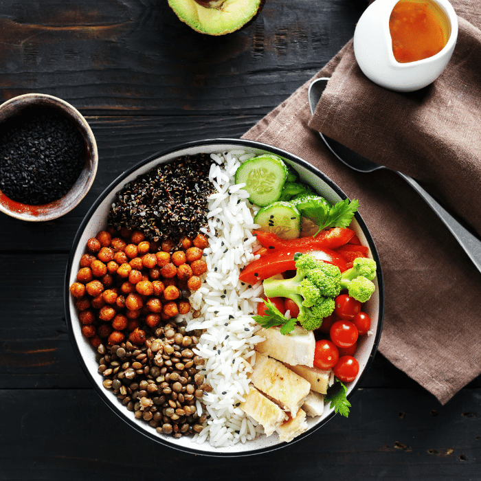 Overhead buddha bowl of rice, lentils, chickpeas, quinoa, tofu, broccoli, cucumber and tomatoes