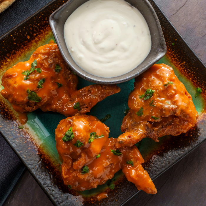 Buffalo chicken wings in orange sauce with parsley beside a bowl of creamy blue cheese dip