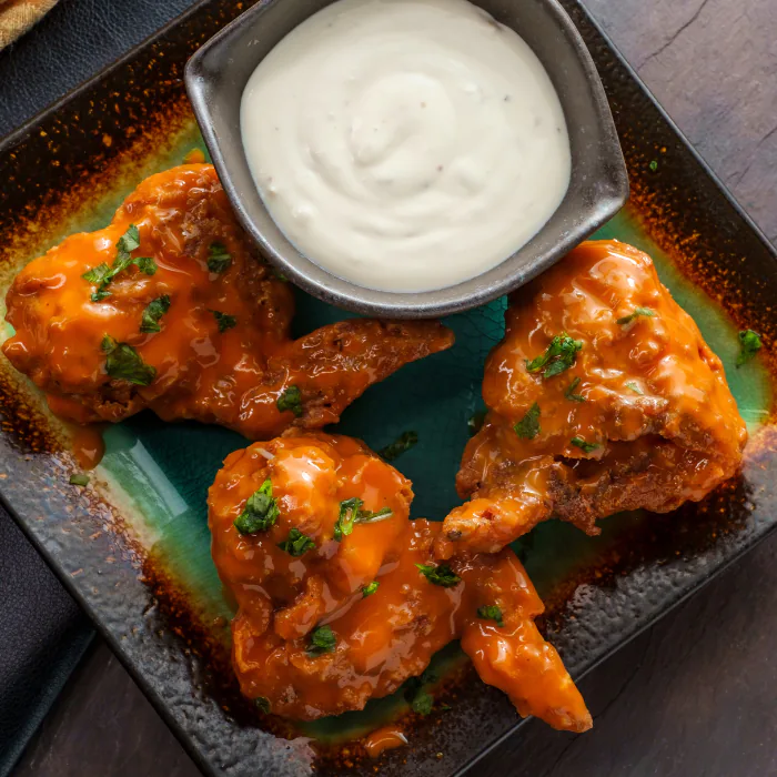 Buffalo chicken wings in orange sauce with parsley beside a bowl of creamy blue cheese dip