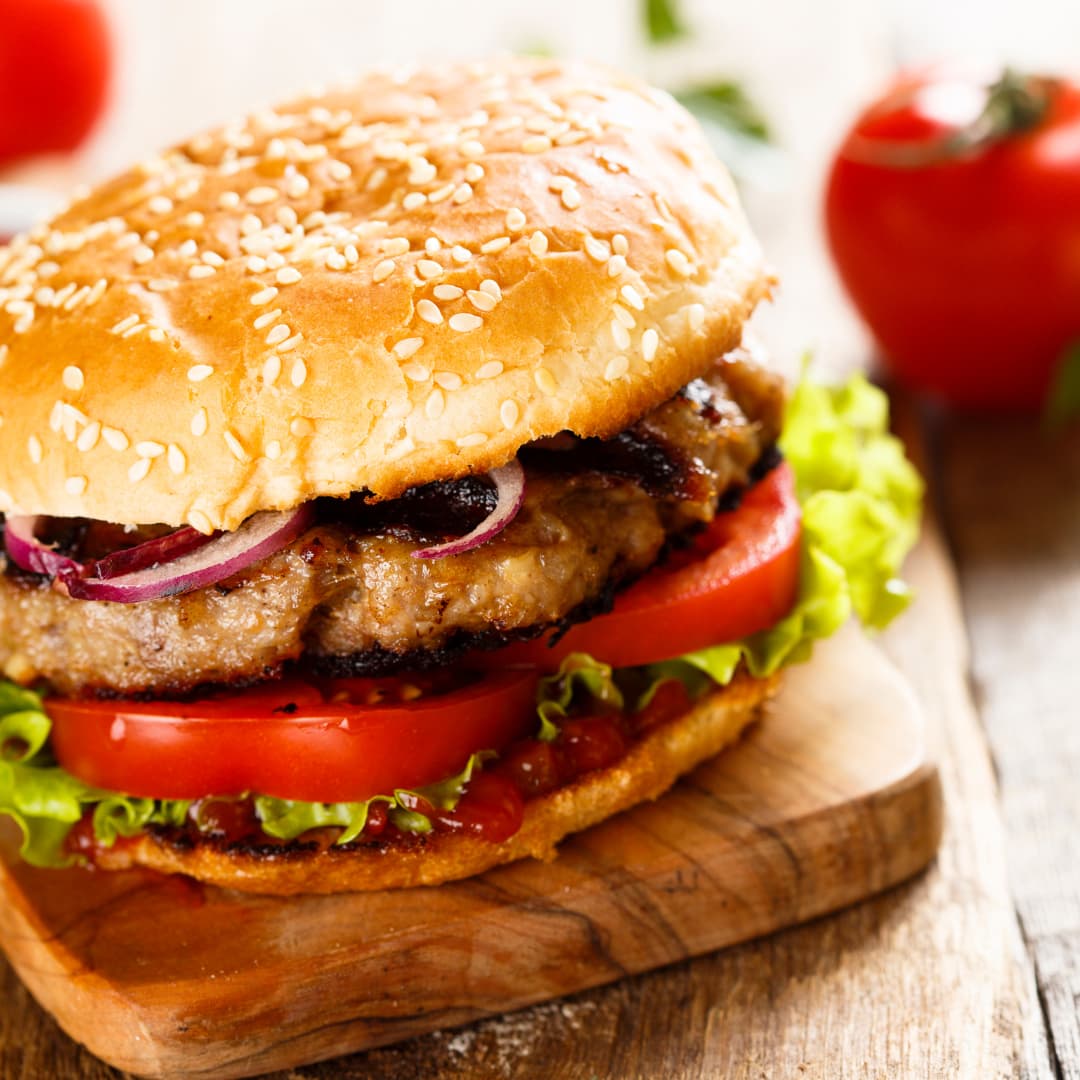 Burger on a sesame seed bun stacked with lettuce, tomato and red onion on a wooden board