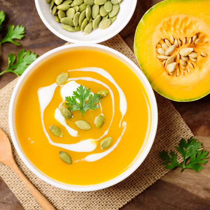 Bowl of butternut bisque swirled with cream and topped with pumpkin seeds, halved squash alongside