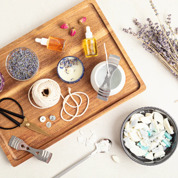 Candle making supplies on a wooden board with lavender, essential oils, wax flakes, wicks and twine