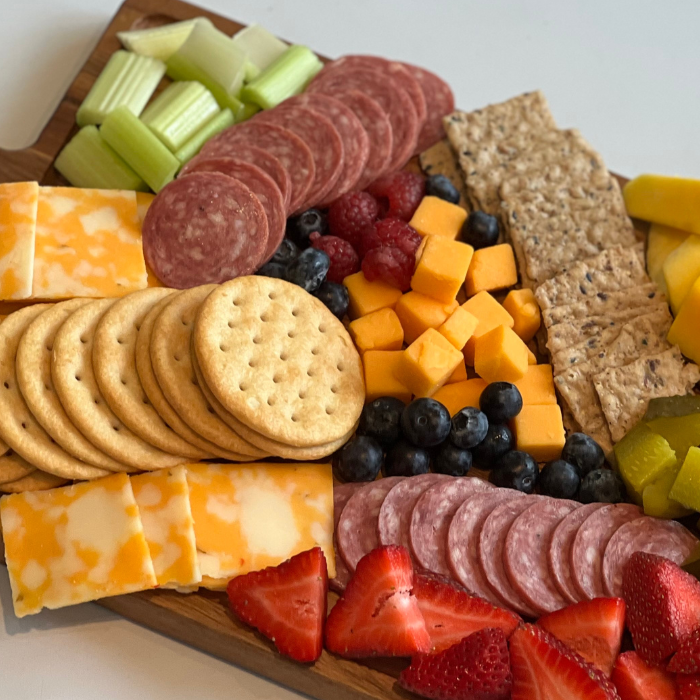 Charcuterie board with salami, cheddar cubes, crackers, strawberries, blueberries and celery