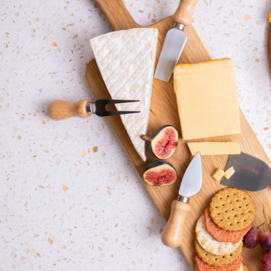 Wooden board with a brie wedge, cheddar, fresh figs, crackers and a set of cheese knives