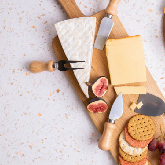 Wooden board with a brie wedge, cheddar, fresh figs, crackers and a set of cheese knives