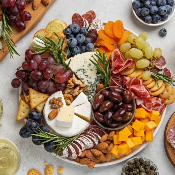 Charcuterie board of brie, blue cheese, cheddar, salami, grapes, berries, olives, crackers and nuts