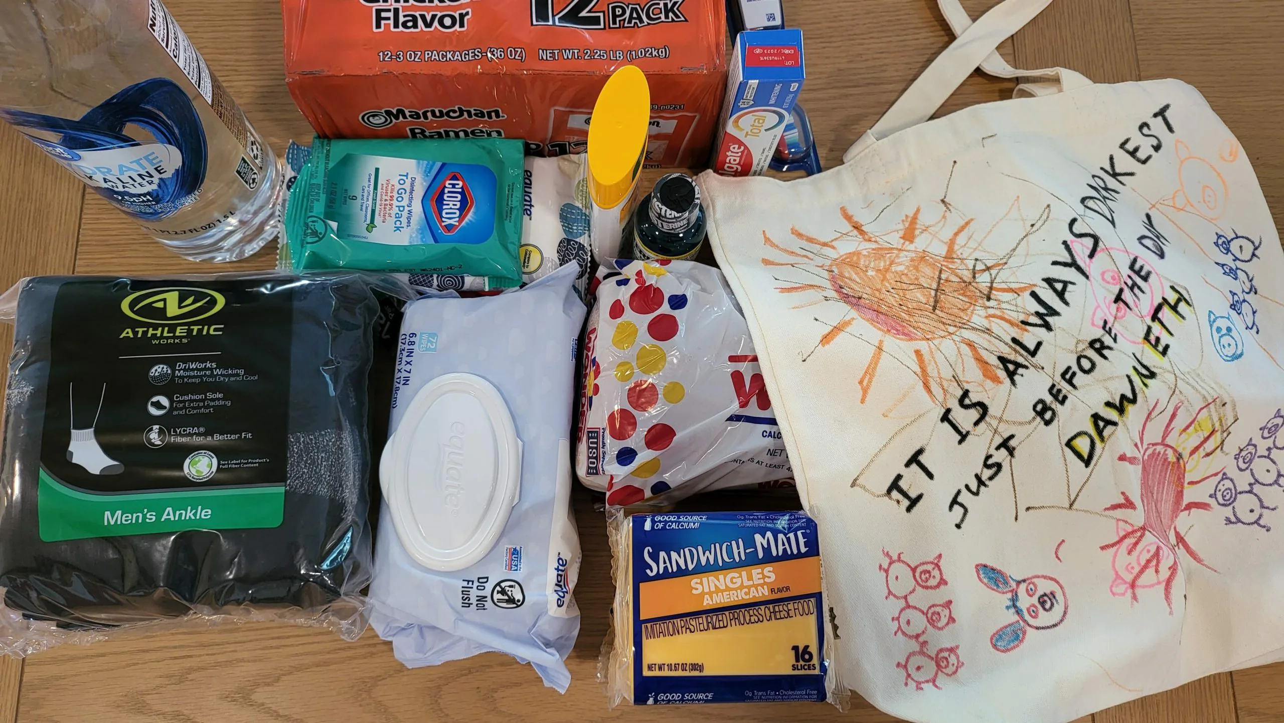 Donated soda, wipes, socks and sandwich bags laid out beside a hand-painted canvas tote bag