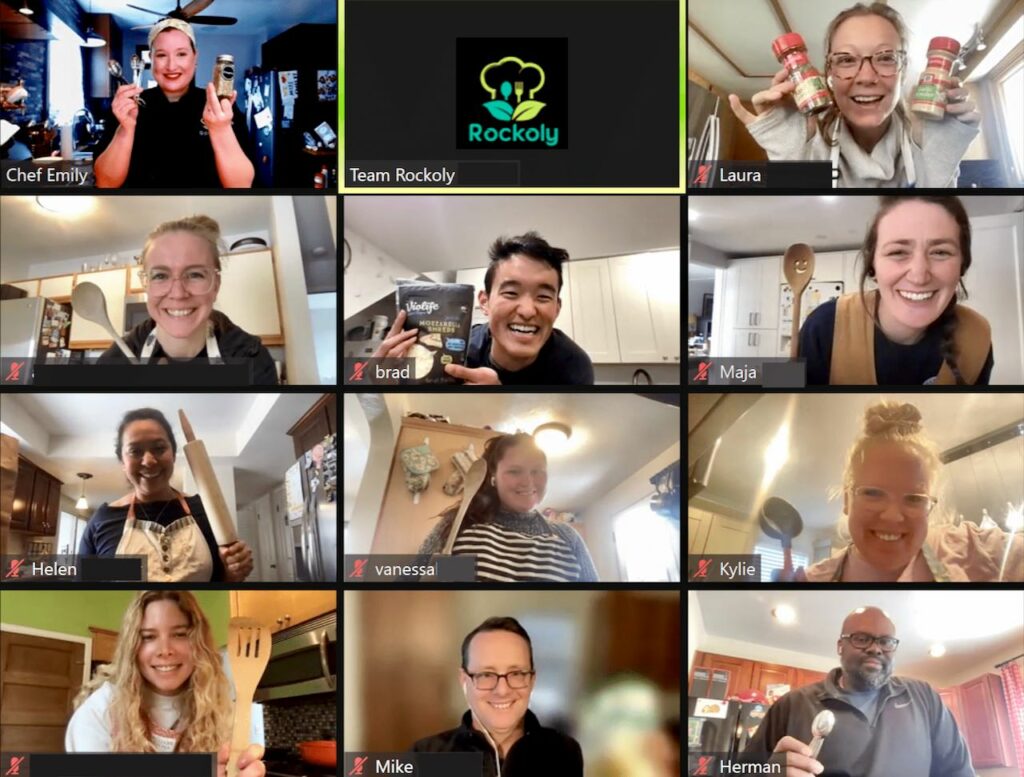Chef Emily and nine coworkers on a video call cooking class, holding up spice jars and wooden spoons