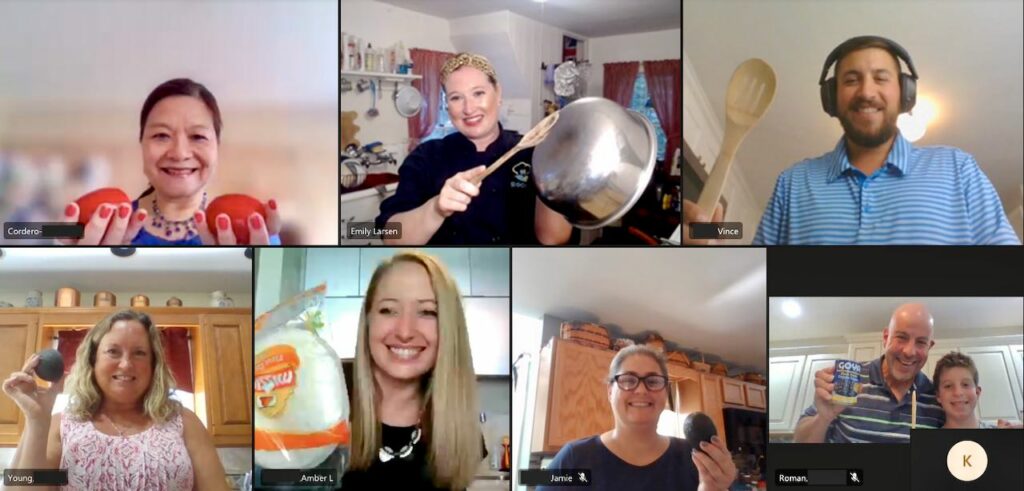 Chef Emily and coworkers on a video-call cooking class, holding up tomatoes, pans and wooden spoons