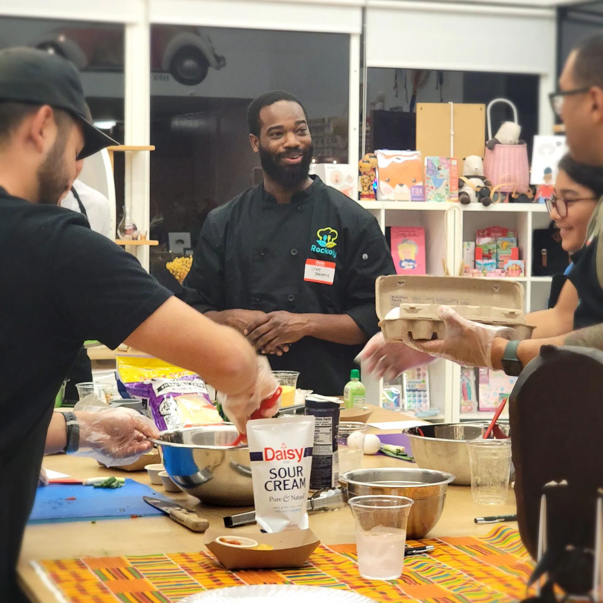 Chef in a Rockoly polo leading an in-person cooking event as guests mix ingredients at a long table