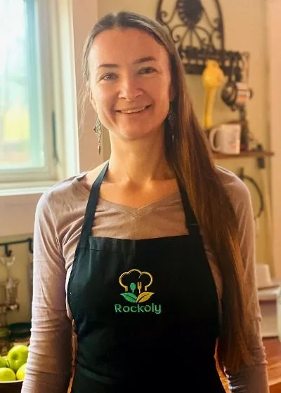 Chef Katya with long hair smiling in a black Rockoly apron in a sunlit home kitchen