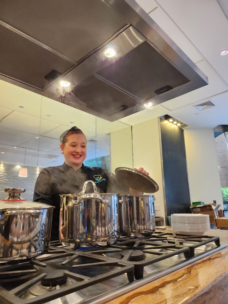 Chef lifting the lid from a stockpot on a gas range in an open event kitchen