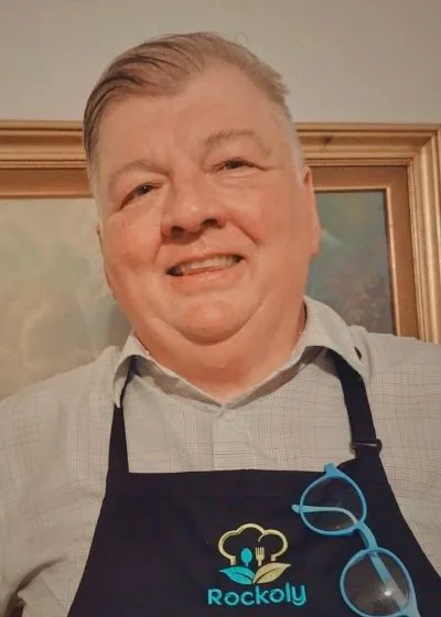Chef Mark smiling in a blue Rockoly apron with a pair of glasses clipped to the strap