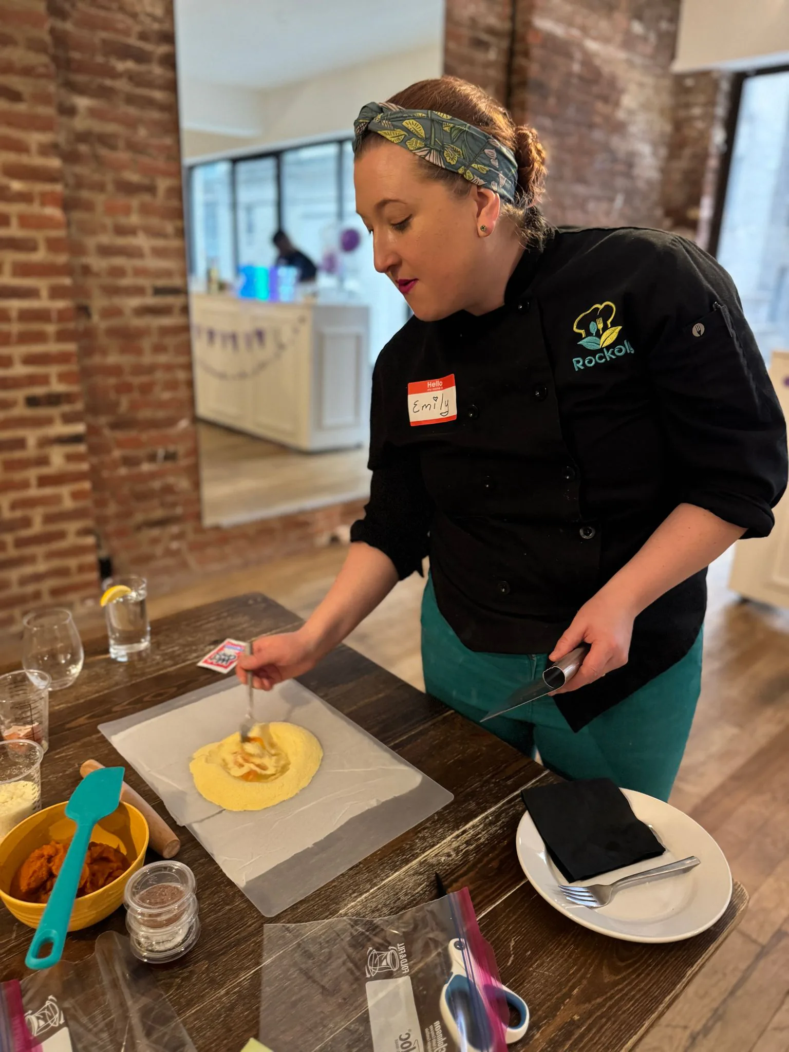 Chef in a black chef jacket works a round sheet of fresh pasta dough at a workshop table