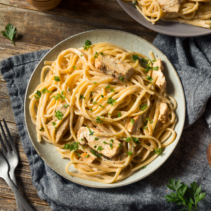 Plate of creamy fettuccine alfredo with sliced chicken and chopped parsley