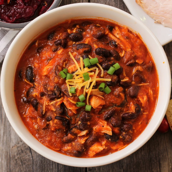 Bowl of chili with black beans, shredded meat, grated cheese and sliced scallions