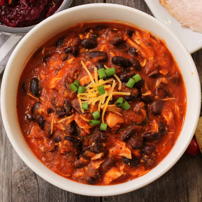 Bowl of chili with black beans, shredded meat, grated cheese and sliced scallions
