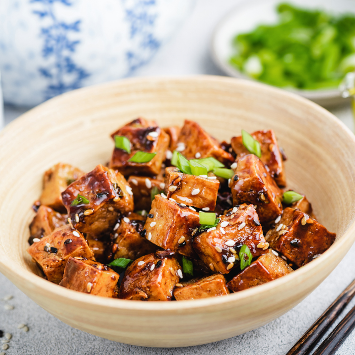 Crisped tofu cubes tossed in chili oil with scallions in a pale wooden bowl