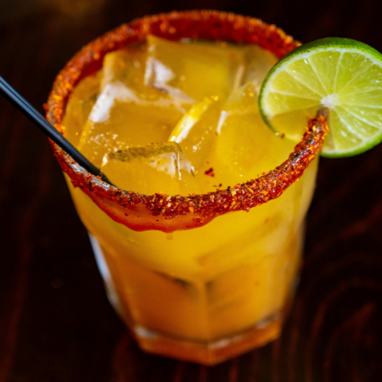 Orange cocktail over ice in a chili-salt rimmed glass, garnished with a lime wheel