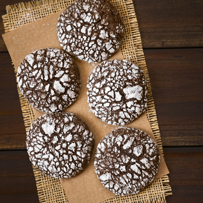 Chocolate crinkle cookies dusted with powdered sugar on parchment over a dark wooden table