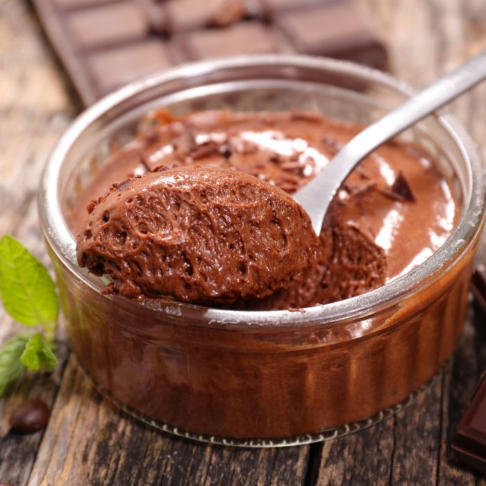 Spoonful of dark chocolate mousse lifted from a glass ramekin, with fresh mint alongside