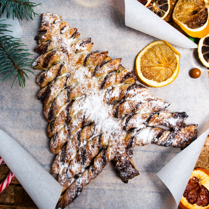Chocolate puff pastry Christmas tree dusted with powdered sugar beside dried orange slices and pine