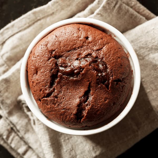 Chocolate souffle baked in a white ramekin, cracked across the top, resting on a linen cloth