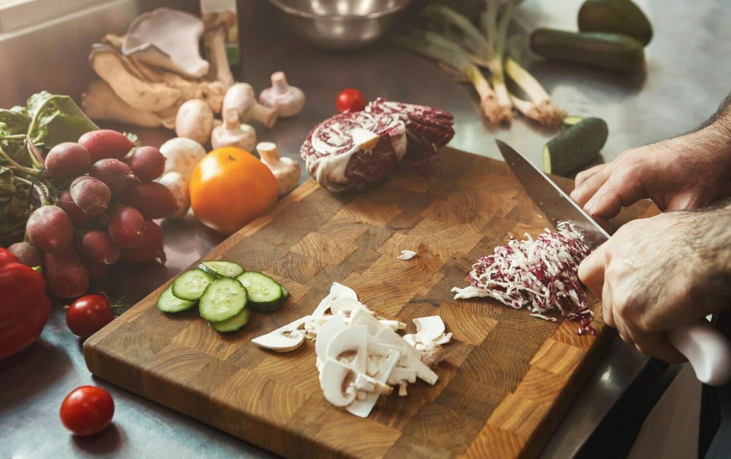 Hands slicing radicchio on a wooden board with mushrooms, cucumber, grapes and tomatoes