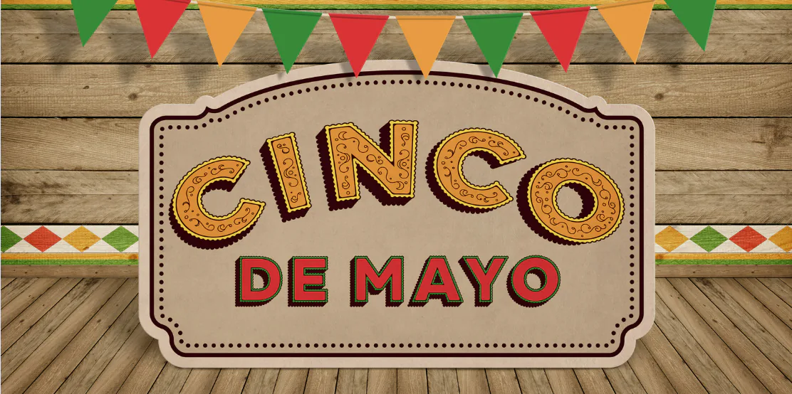 Cinco de Mayo sign on a wooden wall hung with papel picado bunting