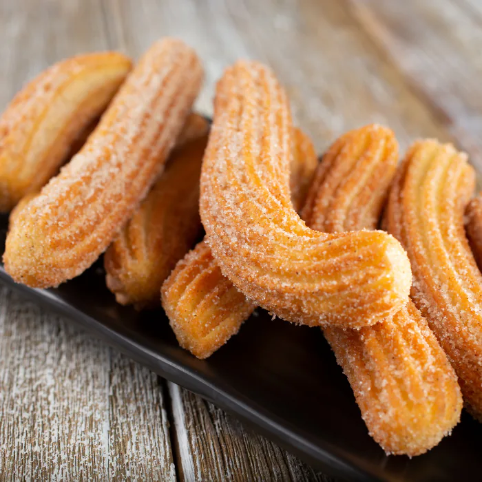 Pile of cinnamon sugar coated churros on a black tray over weathered wood