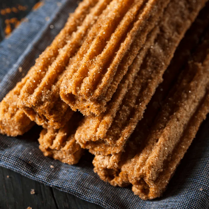 Stack of freshly fried churros coated in cinnamon sugar on a blue cloth